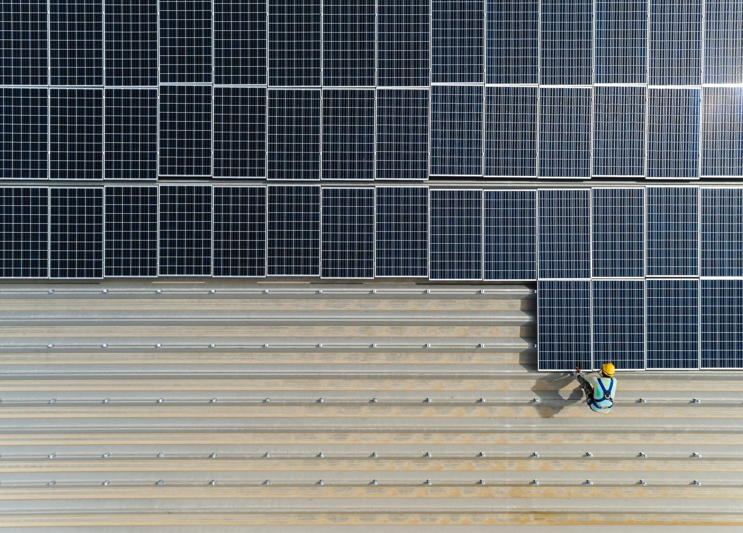 A technician on a roof covered with solar panels, seen from above